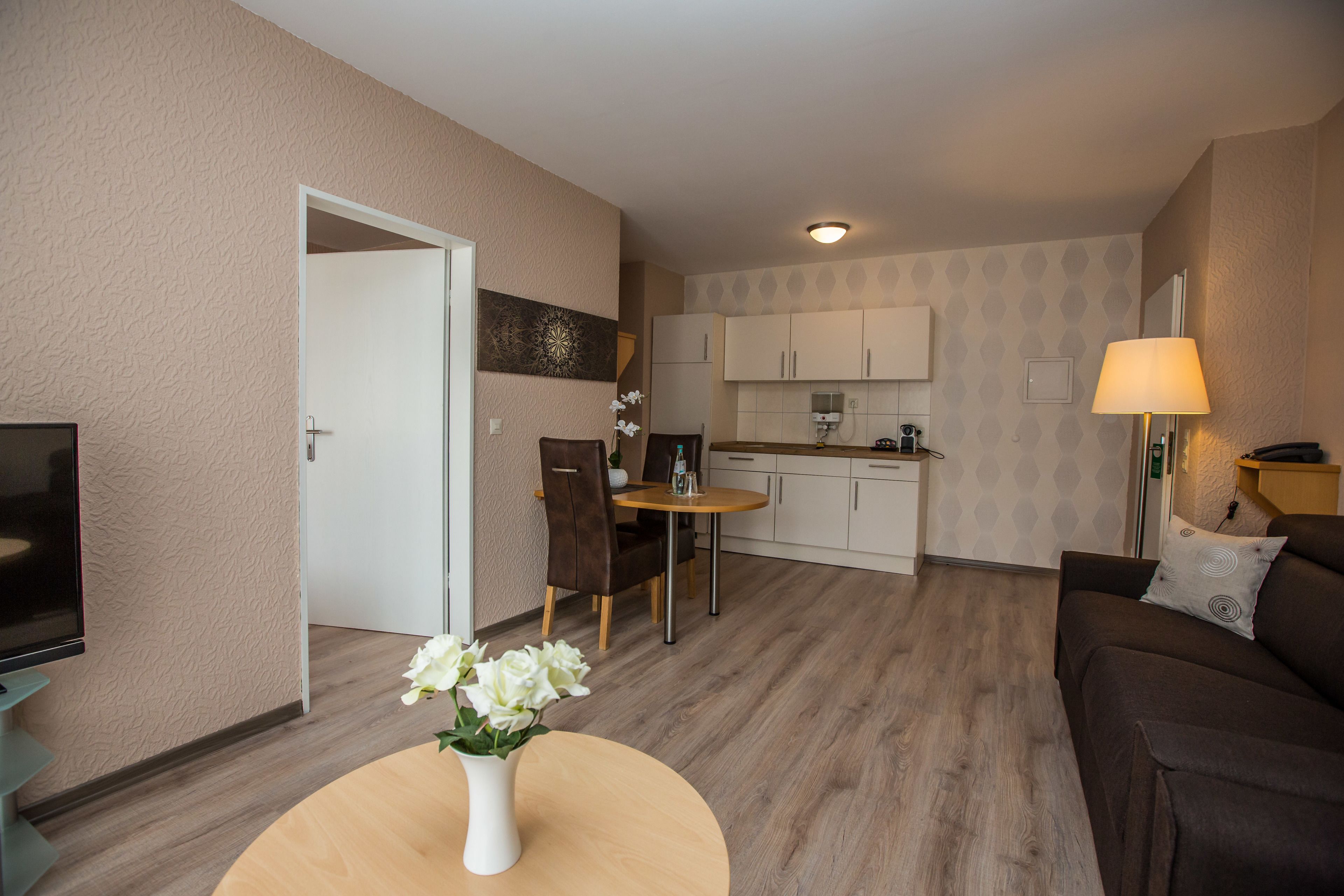 Ein modernes Wohnzimmer mit Sofa, Fernseher, Esstisch mit Stühlen und einer Küchenzeile mit Schränken und Arbeitsplatte.