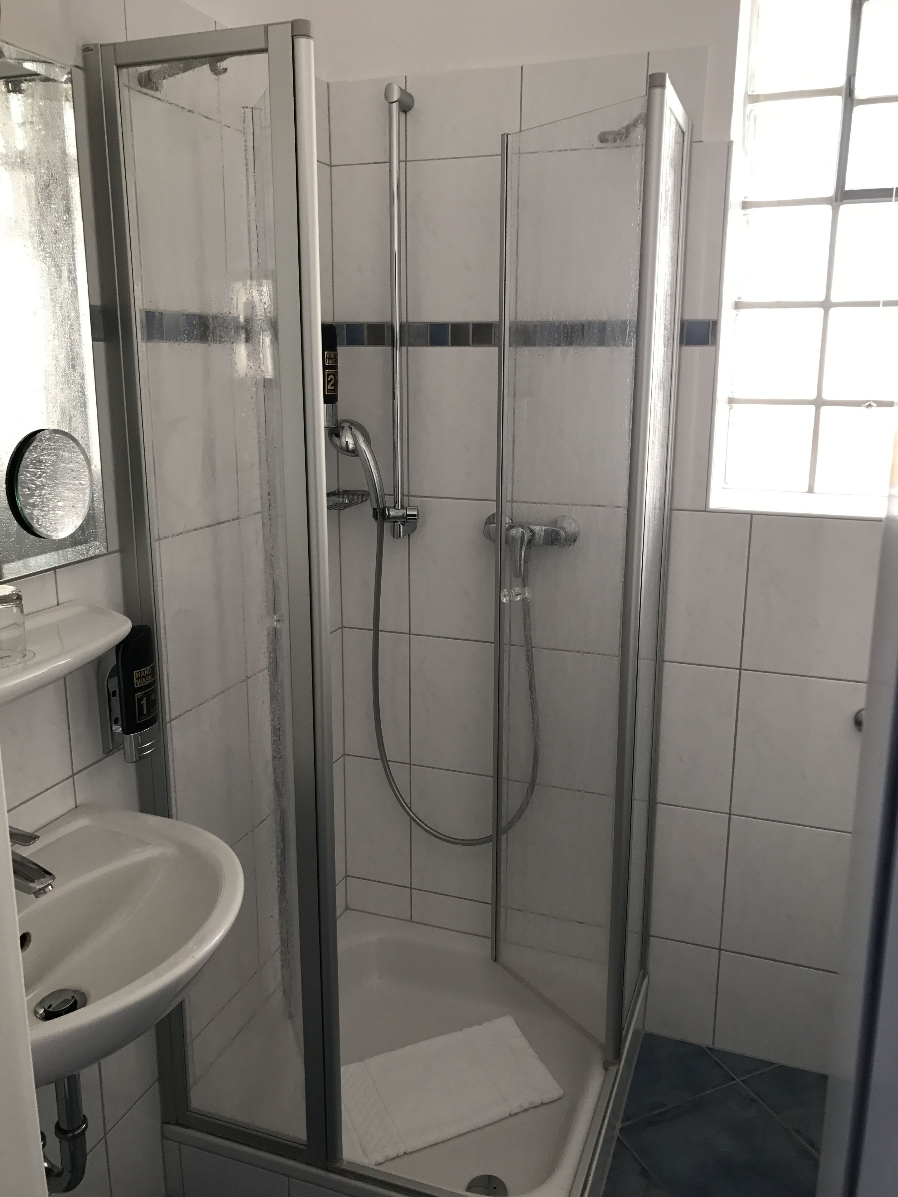 Un box de ducha con paredes de vidrio, con un cabezal de ducha y un grifo de mano.