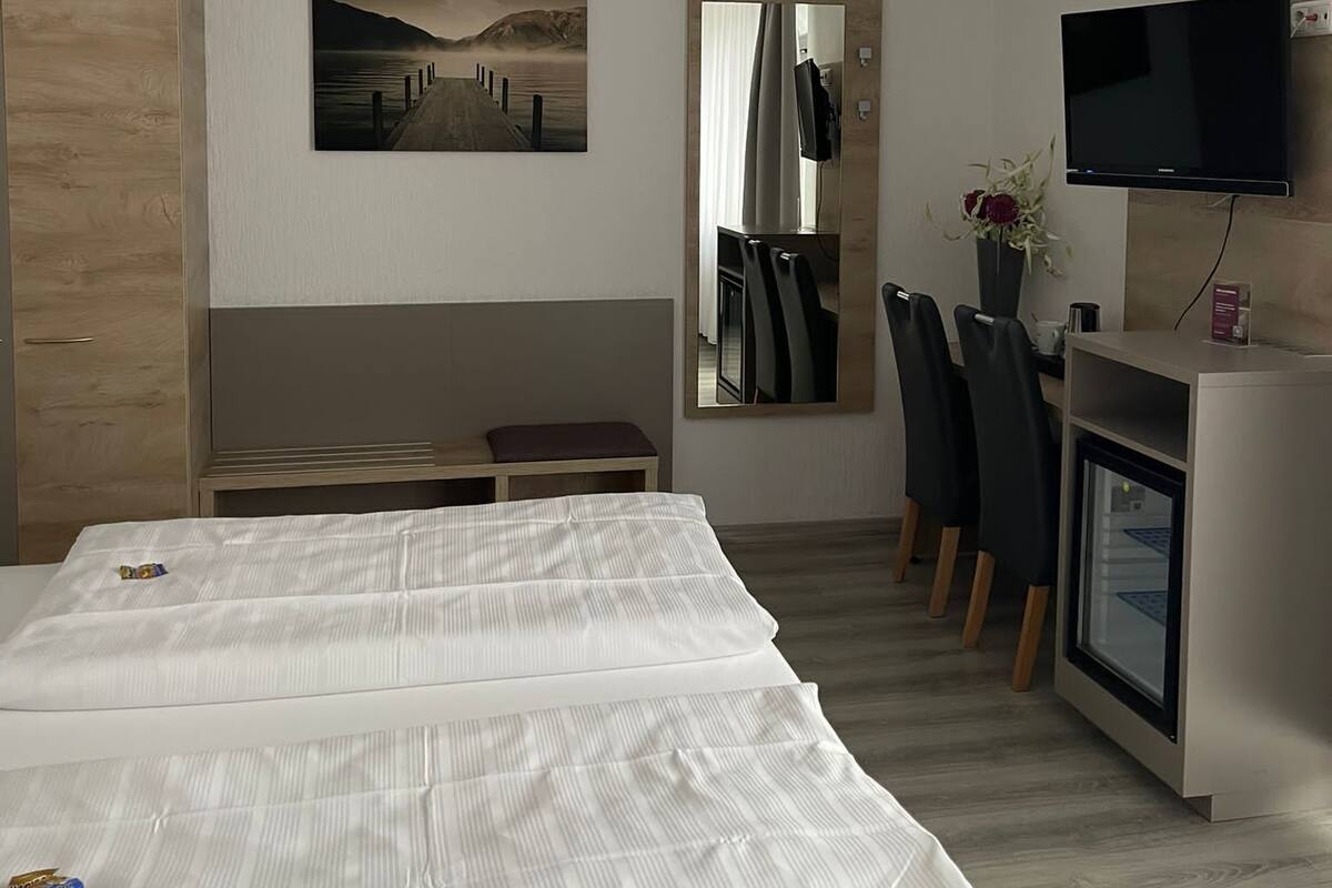 Una habitación de hotel moderna con una cama grande, un escritorio con silla, un televisor y un cuadro en la pared.