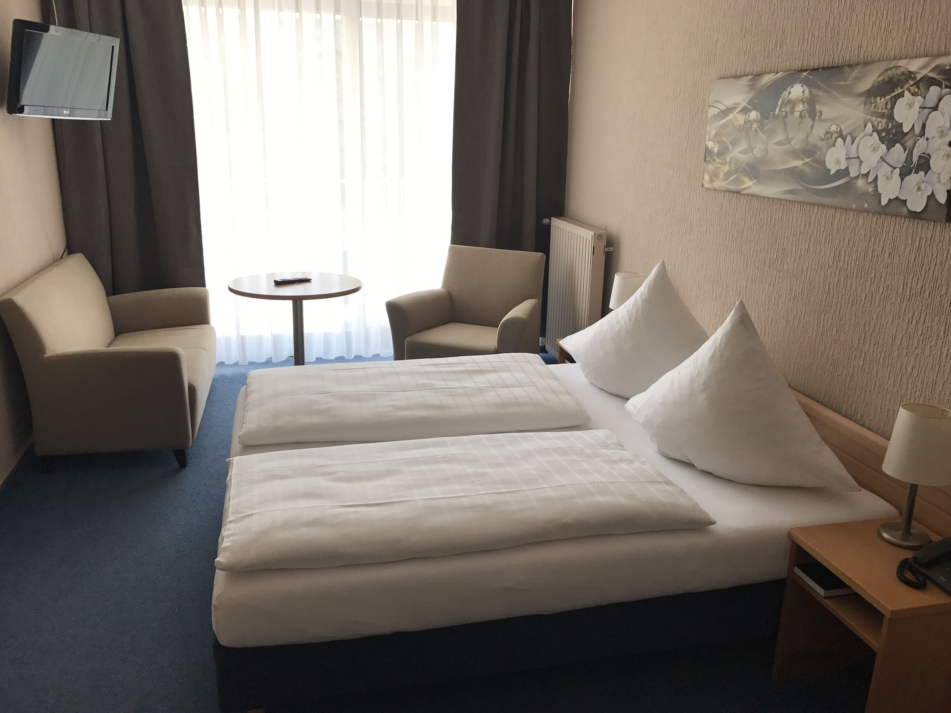 Habitación de hotel con una cama grande, dos sillones, una mesita y un televisor montado en la pared.