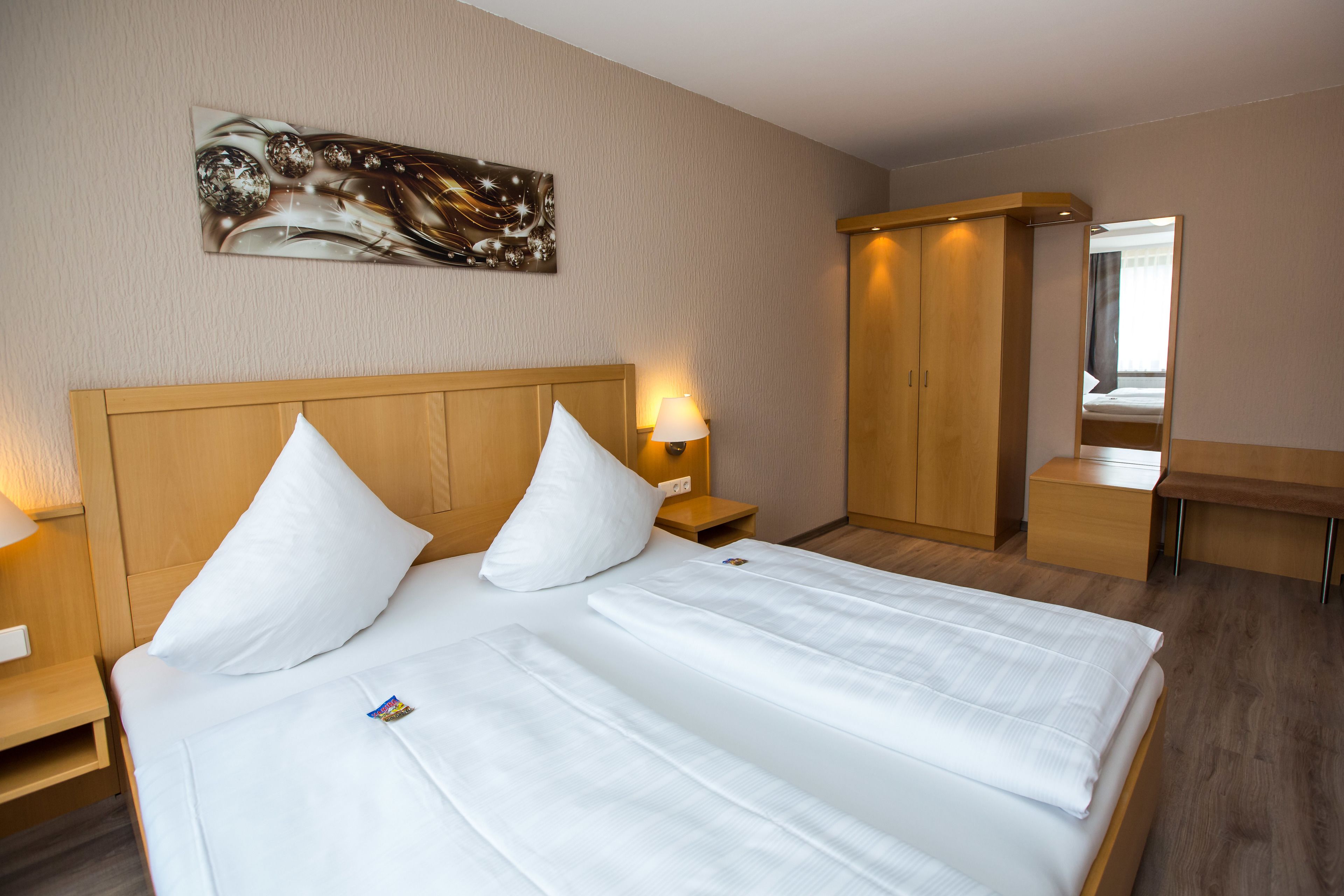 Ein Hotelzimmer mit einem großen Bett, einem hölzernen Kopfteil, einem Nachttisch mit Lampe, einem Kleiderschrank und einem Spiegel.