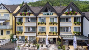A hotel with a yellow facade, multiple balconies with flower boxes, outdoor seating, and a visible entrance. - Hotel Traumblick (Cochem)