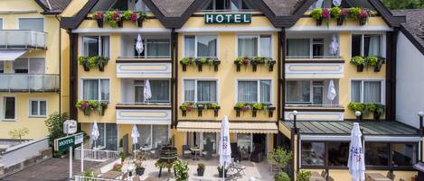 A hotel with a yellow facade, multiple balconies with flower boxes, outdoor seating, and a visible entrance.