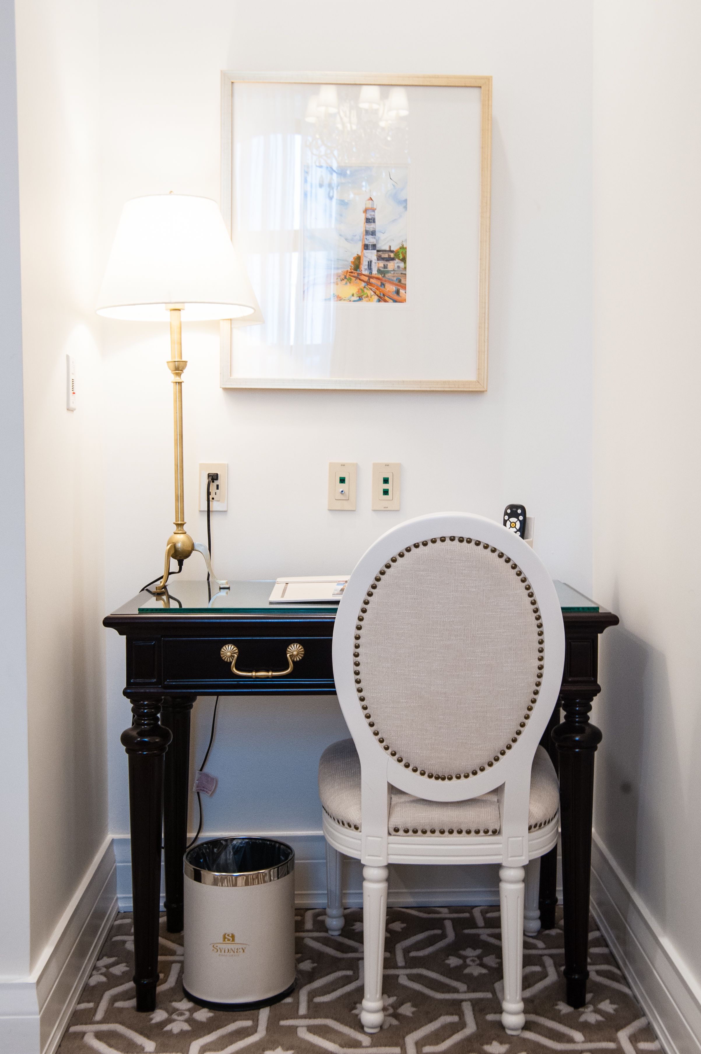A desk with a lamp, a chair, a framed picture, and a trash can.