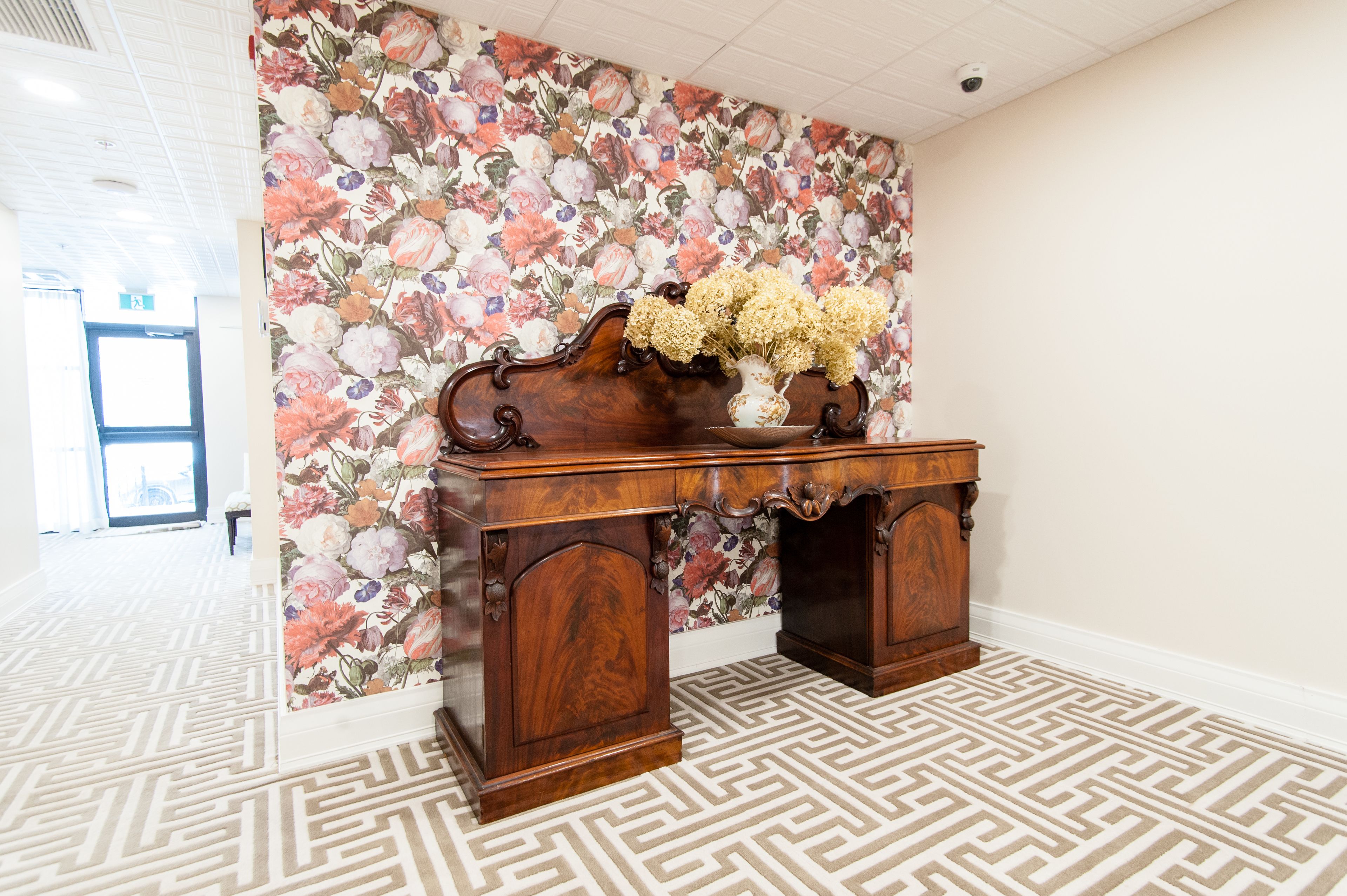 Een houten bureau met bloemen behang en een patroon vloer.
