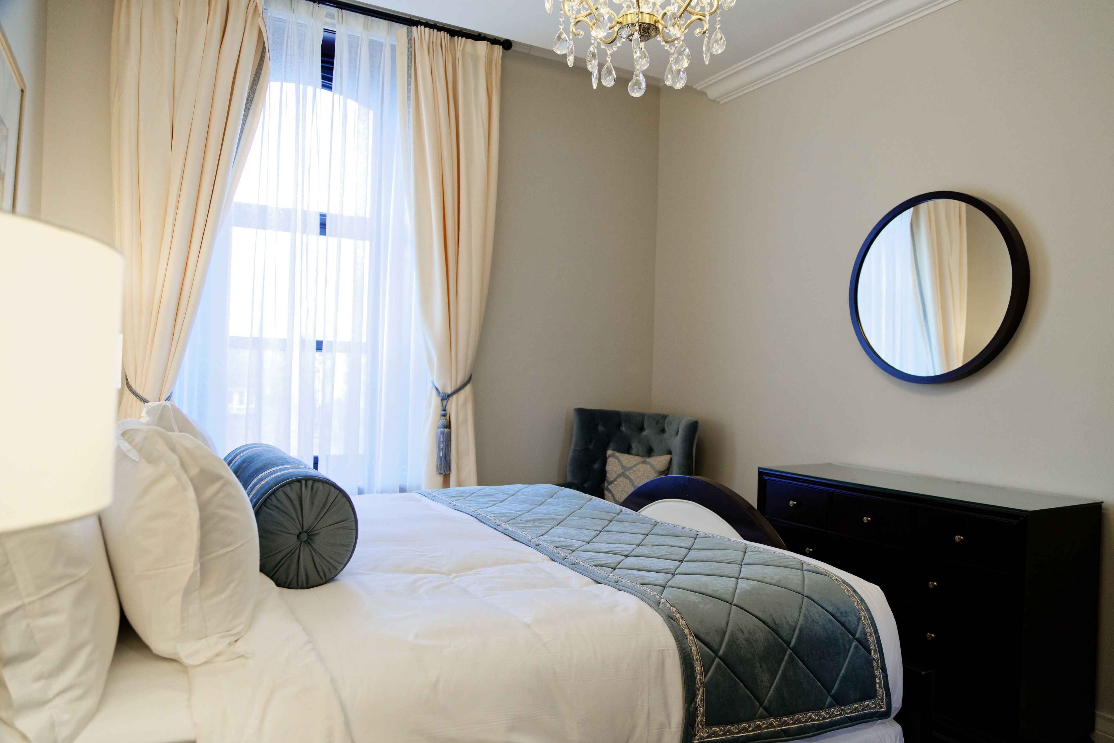 A neatly arranged bedroom with a bed, a dresser, a mirror, and a window with curtains.
