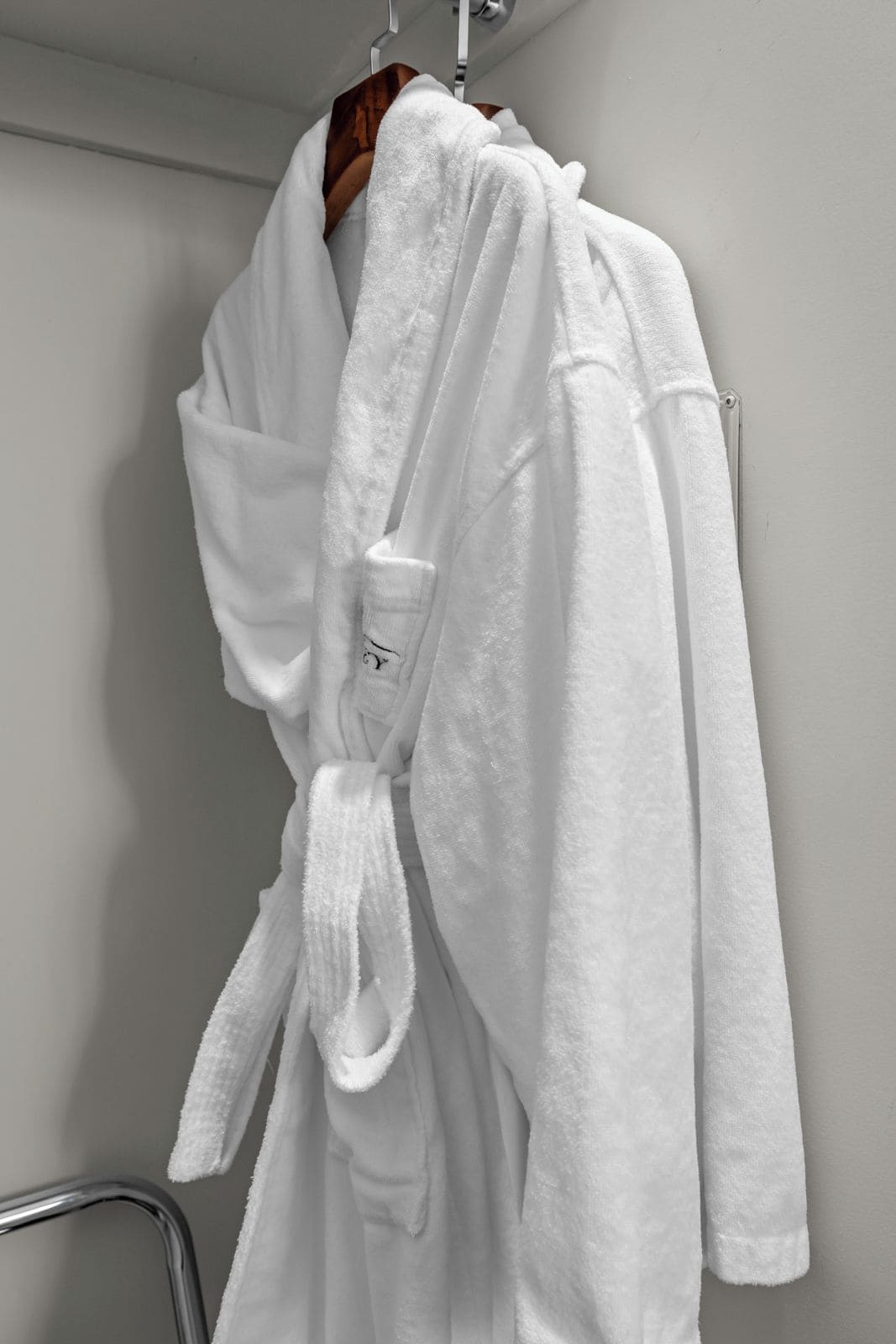 A white bathrobe hanging on a metal rack in a bathroom.