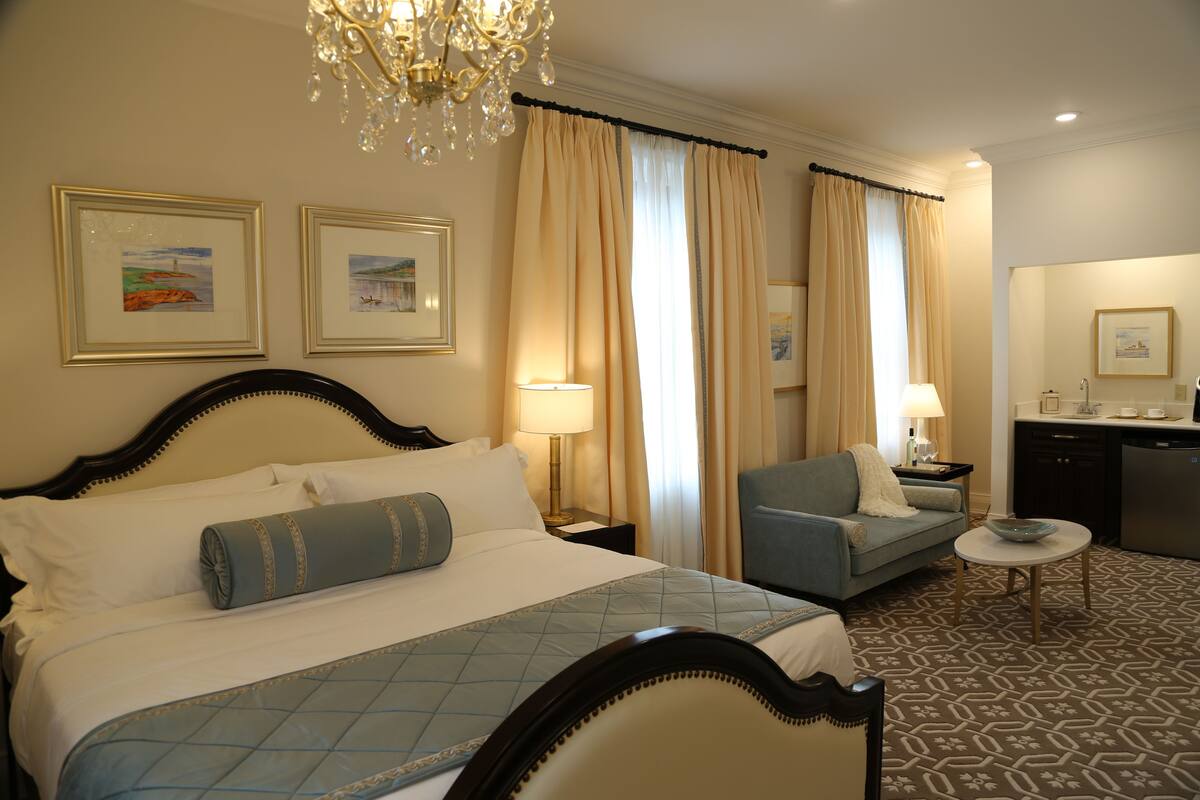 A hotel room with a bed, a sofa, a small table, and a kitchenette.
