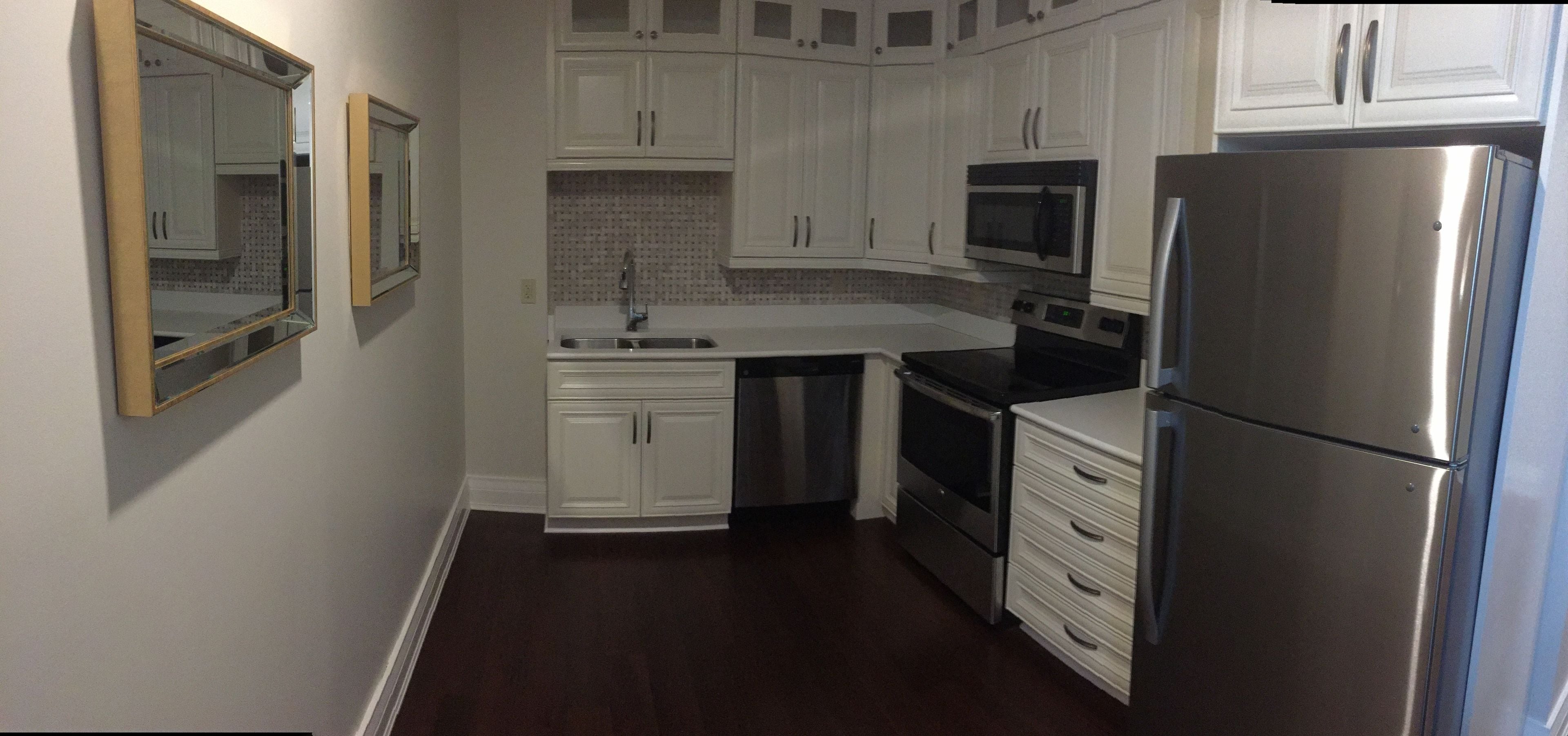 Una cocina compacta con armarios blancos, un refrigerador de acero inoxidable, un microondas y un horno.