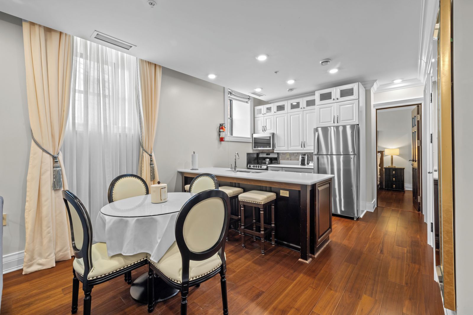 A modern kitchen with white cabinets, a stainless steel refrigerator, and a dining area with a round table and chairs.
