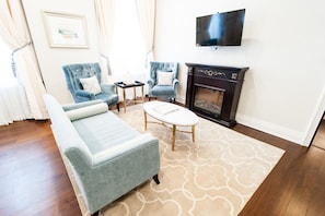 A living room with a sofa, two armchairs, a coffee table, a fireplace, and a TV mounted on the wall.