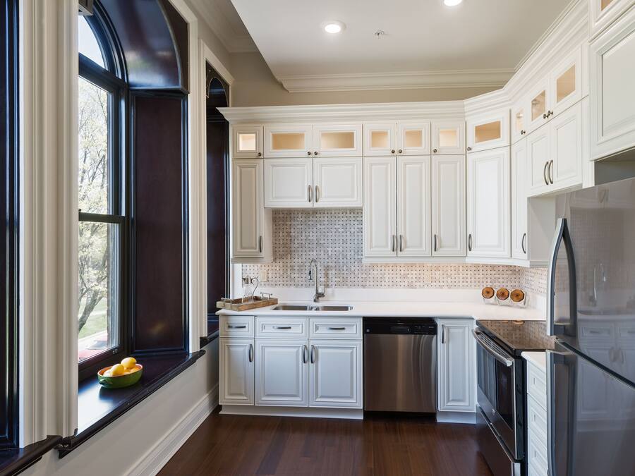 A kitchen with white cabinets, a stainless steel refrigerator, and a window with a bowl of fruit on the windowsill.