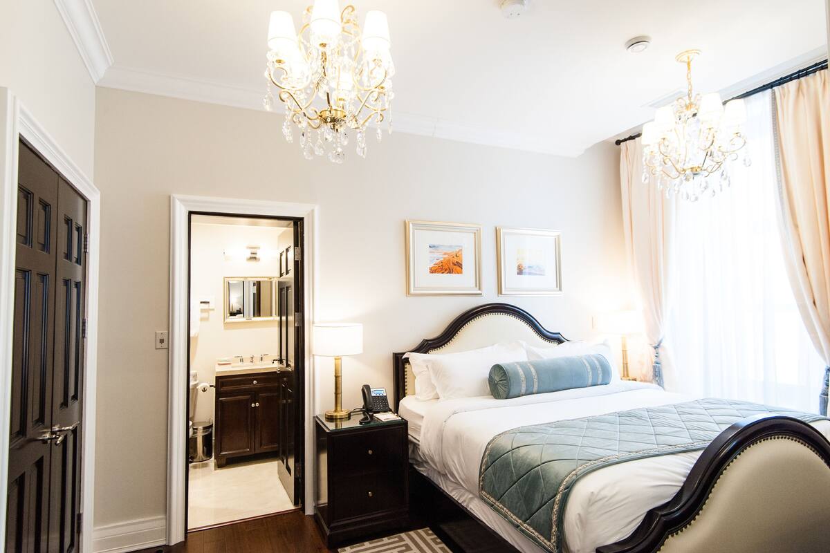A hotel room with a bed, nightstand, dresser, and chandelier.