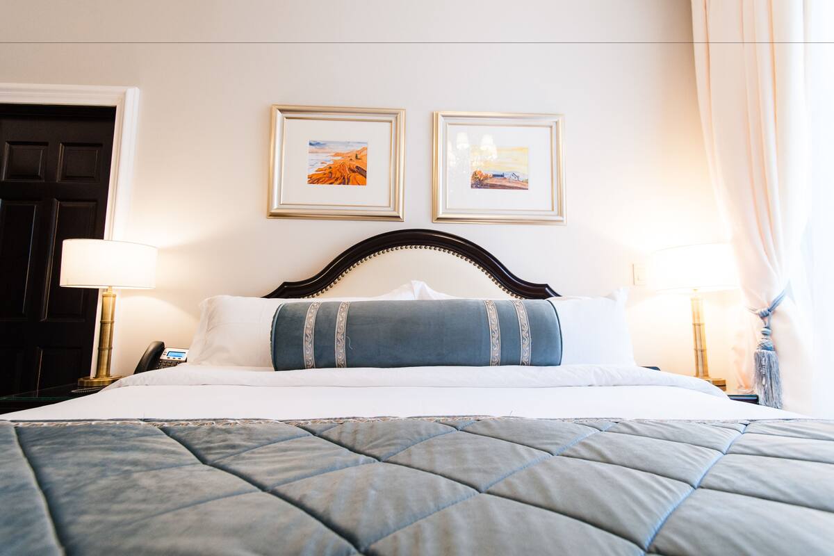 A neatly made bed with a quilted blue and gray bedspread, two framed pictures on the wall, and two bedside lamps.