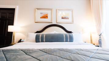 Een net opgemaakt bed met een gewatteerde blauw-grijze spreidek, twee ingelijste foto's aan de muur en twee bedlampen.
