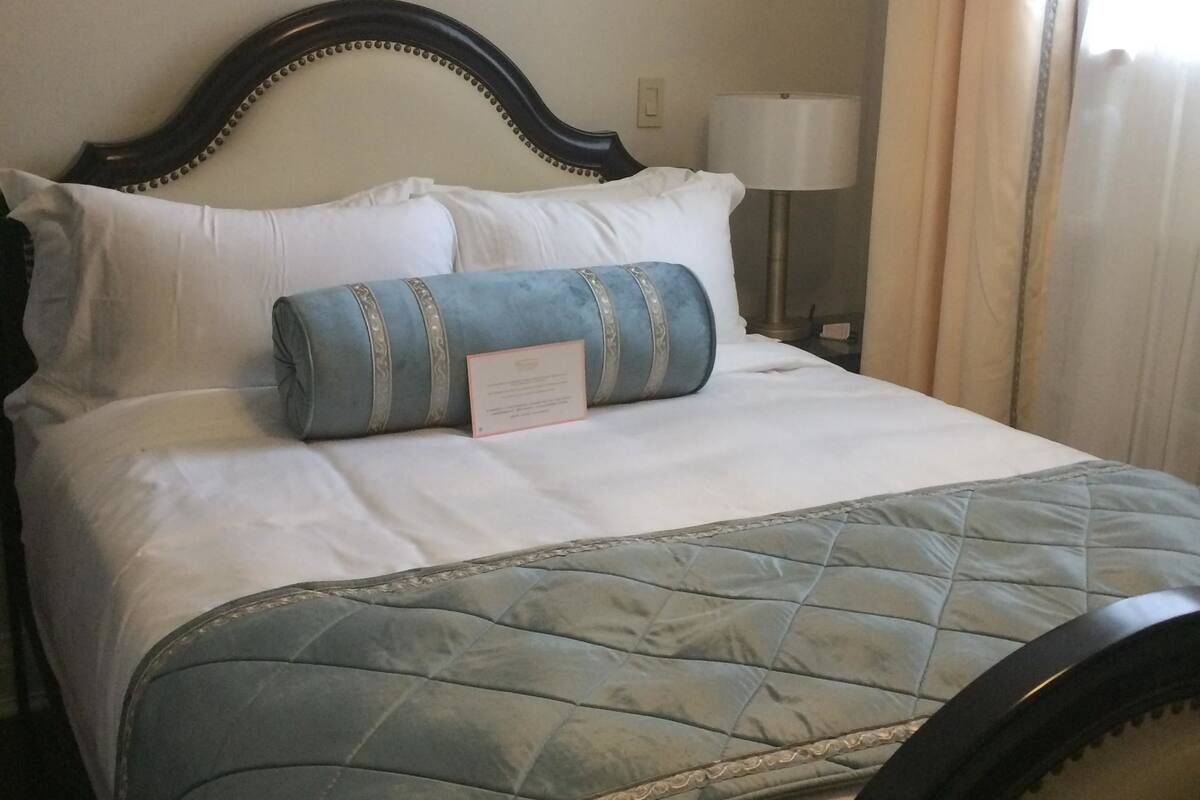 A neatly made bed with a quilted bedspread, a headboard with decorative bead trim, and a bedside lamp.