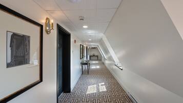 A hallway with patterned flooring, framed artwork on the walls, and a ceiling with recessed lighting and a smoke detector.