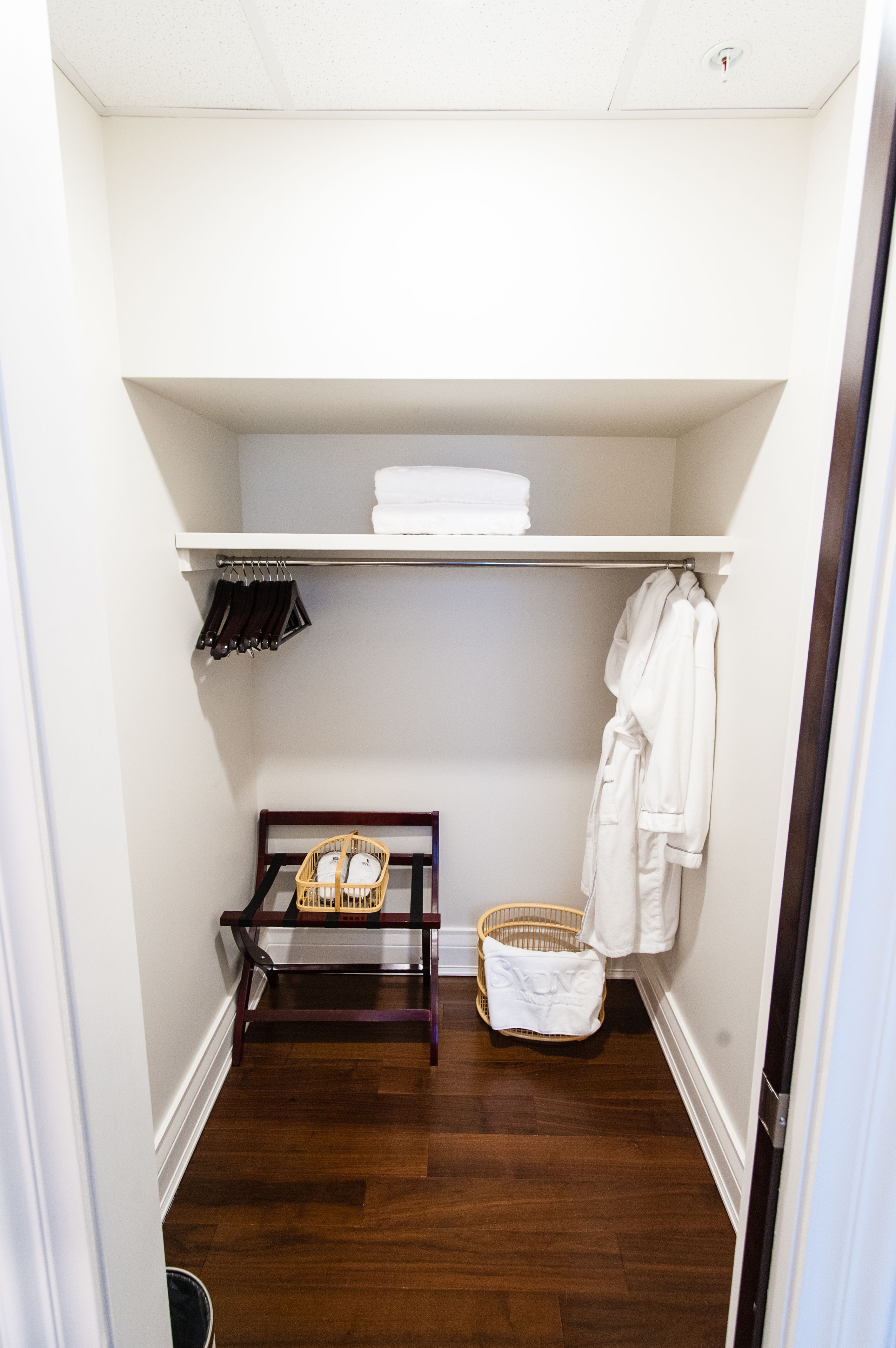 A walk-in closet with a wooden floor, a shelf with folded towels, a wicker basket, and a hanging robe.