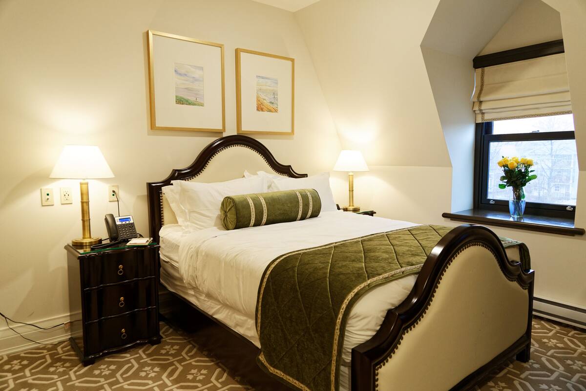 A neatly made bed with a green quilt, two bedside lamps, and a nightstand with a phone.