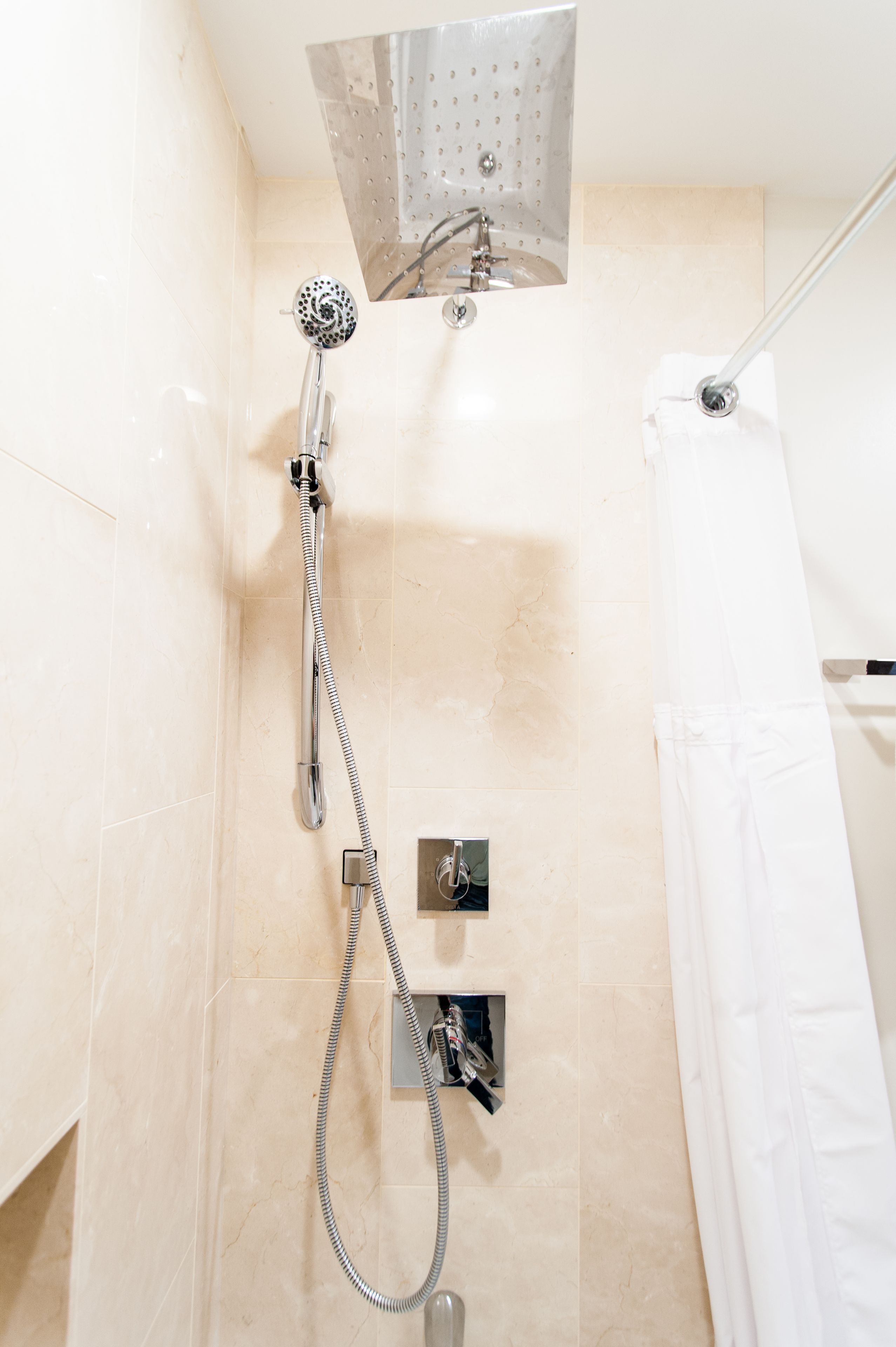 Ducha con cabezal de ducha de mano y panel de control en la pared.