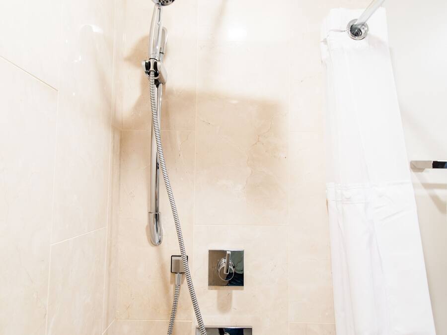 A shower with a handheld showerhead and a wall-mounted control panel.