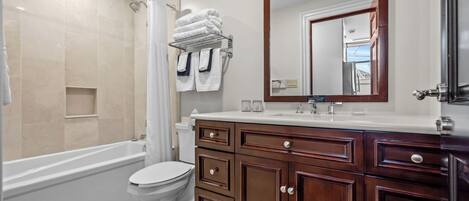 A modern bathroom with a bathtub, toilet, vanity with drawers, and a large mirror.