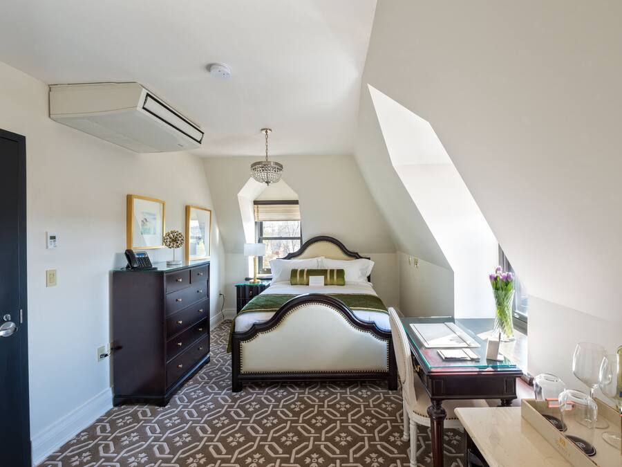 Un dormitorio con una cama grande, un aparador, un escritorio con una silla, una ventana con vistas y una araña.