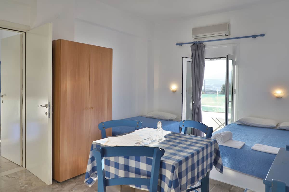 A room with a bed, a table with a checkered tablecloth, a wooden wardrobe, and a window with curtains.
