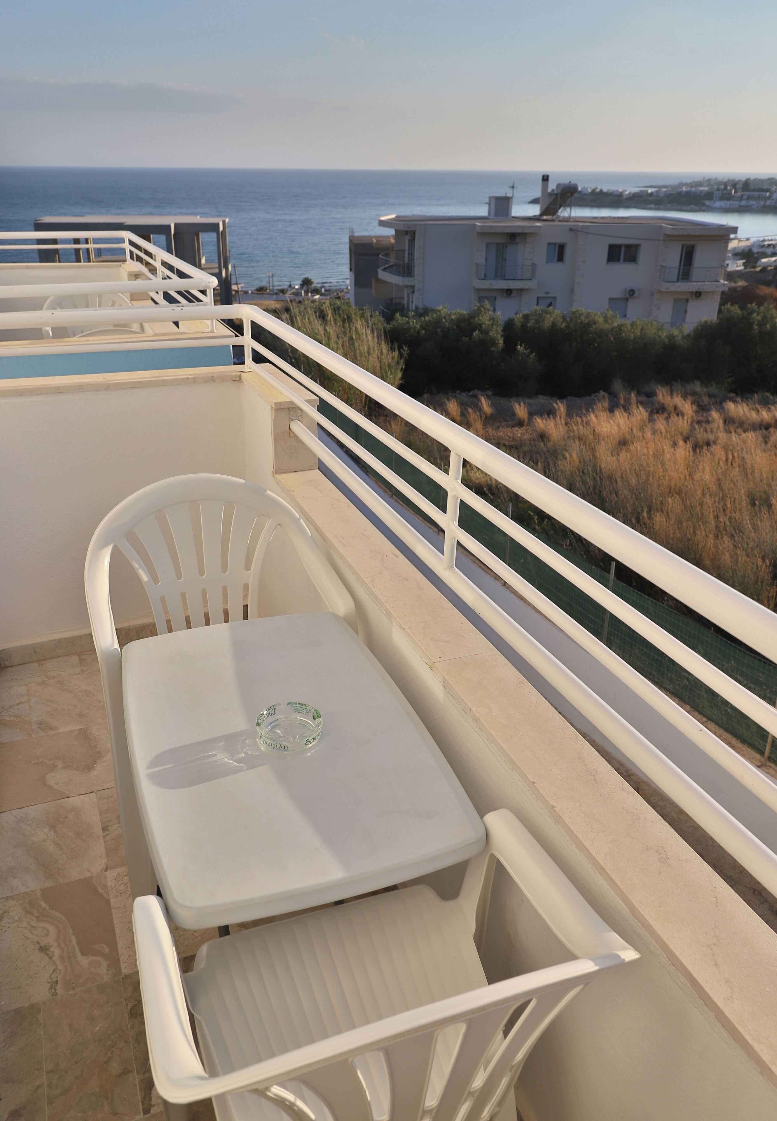 Un balcon avec une table et des chaises, donnant sur une zone côtière avec des bâtiments et une vue sur la mer.