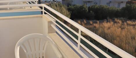 Un balcon avec une table et des chaises, donnant sur une zone côtière avec des bâtiments et une vue sur la mer.