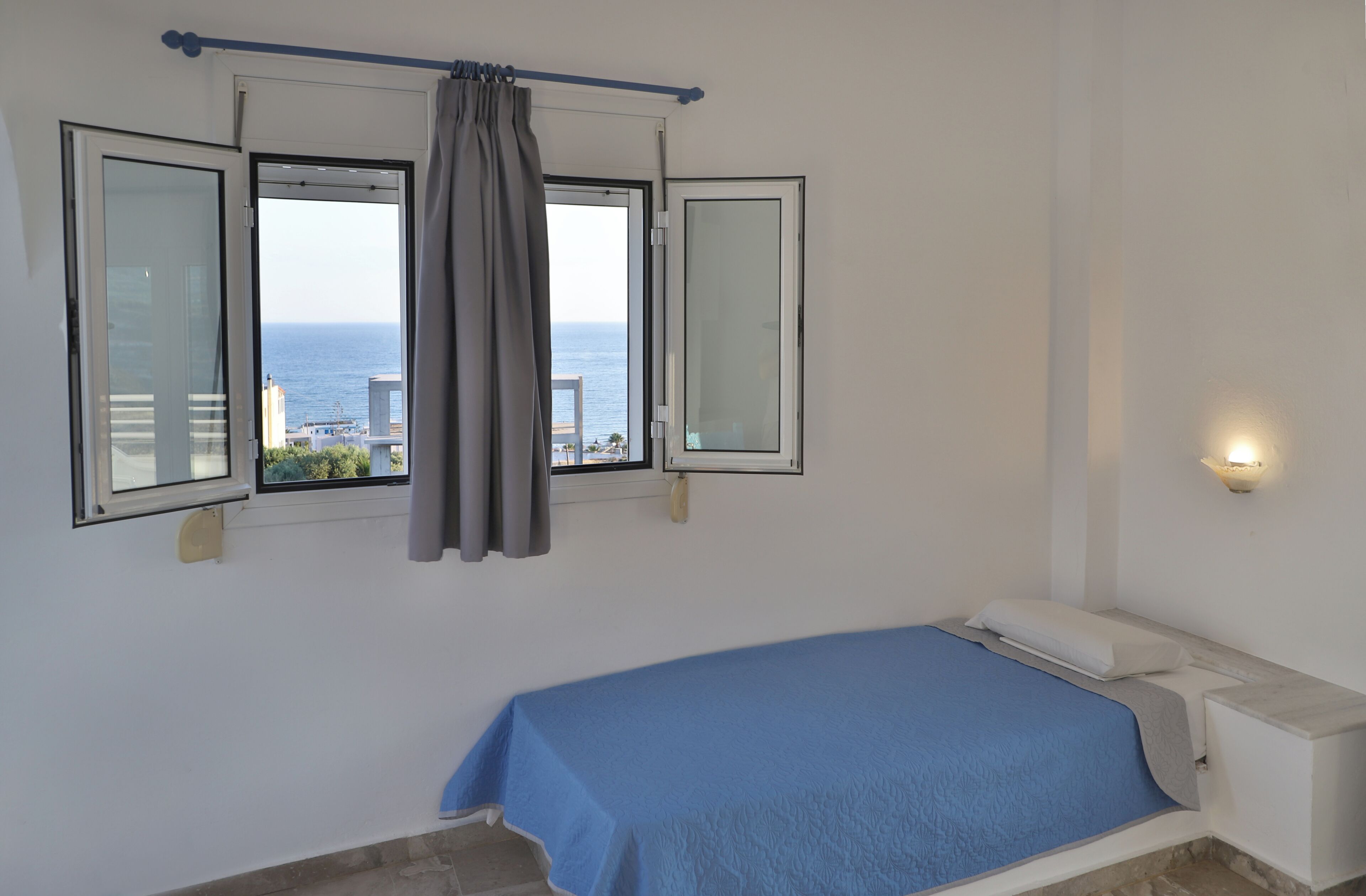 A room with a bed, a window with curtains, and a view of the sea.