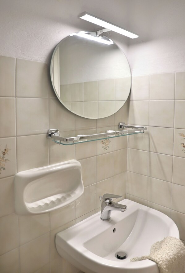 A bathroom with a white sink, a mirror, and a glass shelf.