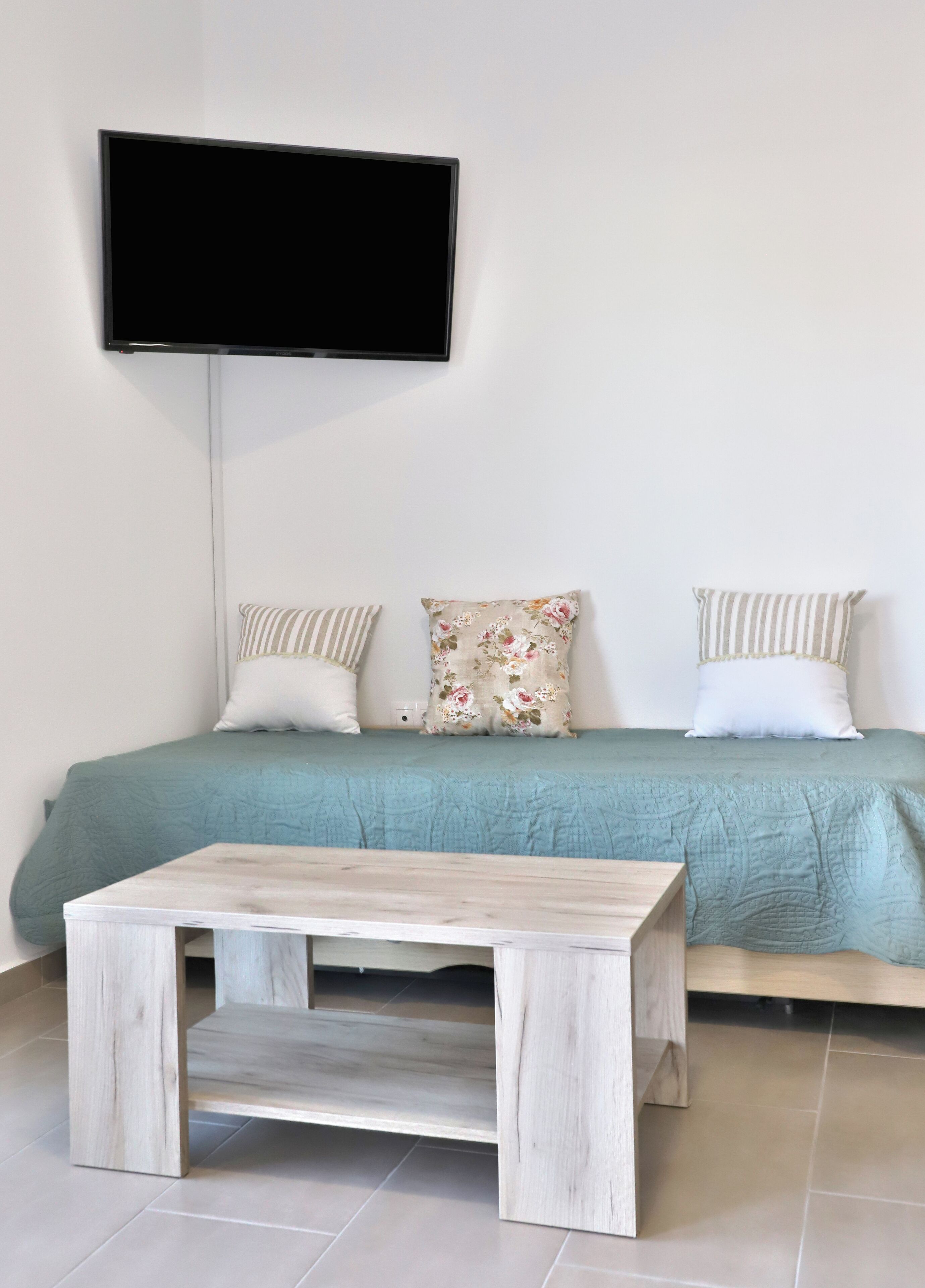 Un dormitorio con cama, televisor de pantalla plana en la pared y una mesa de madera frente a la cama.