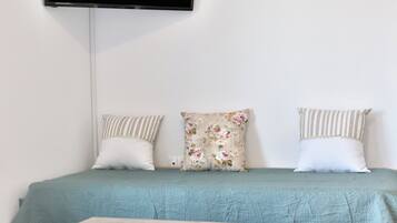 Un dormitorio con cama, televisor de pantalla plana en la pared y una mesa de madera frente a la cama.