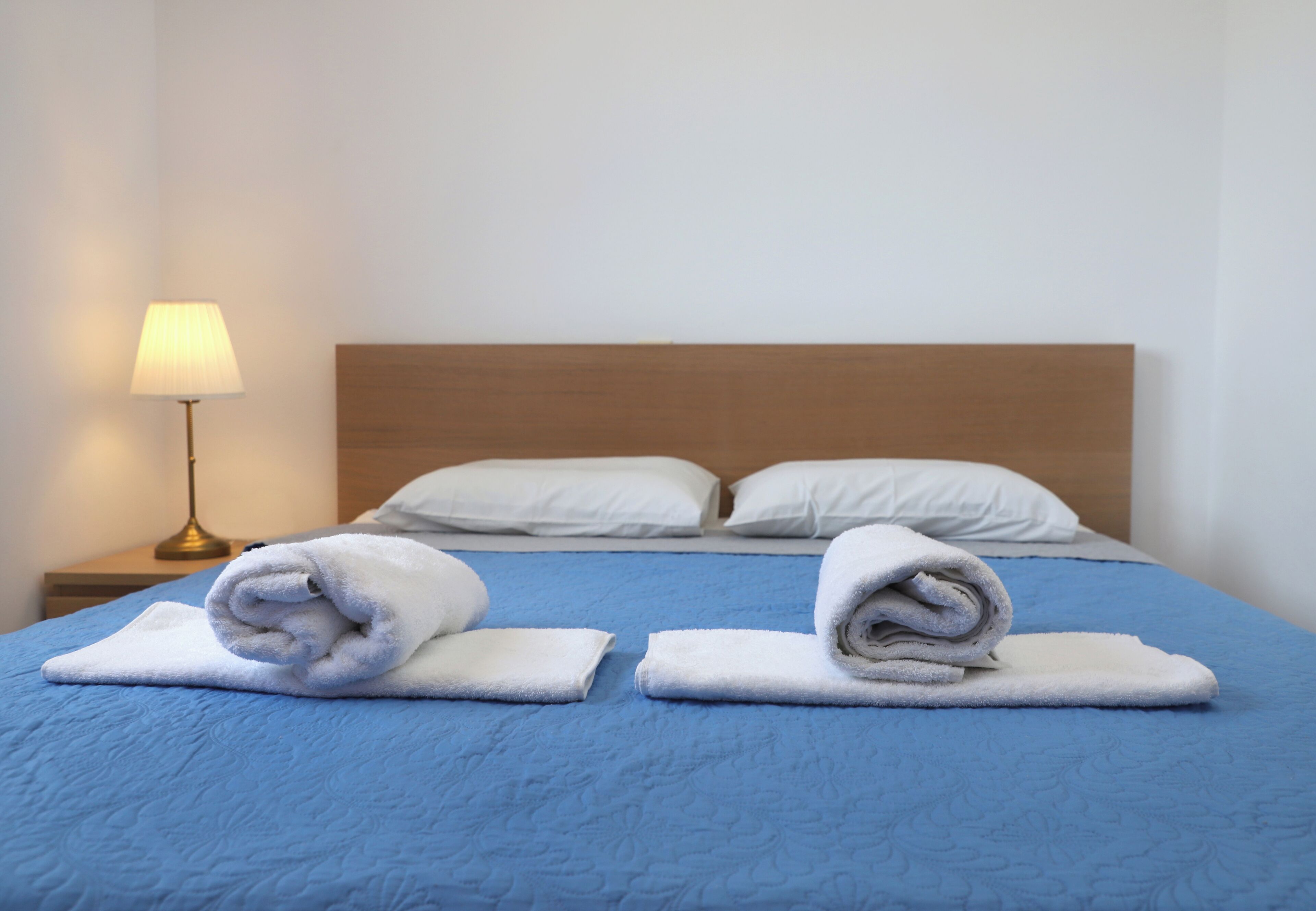 A neatly made bed with blue bedding and two rolled white towels on the bed.