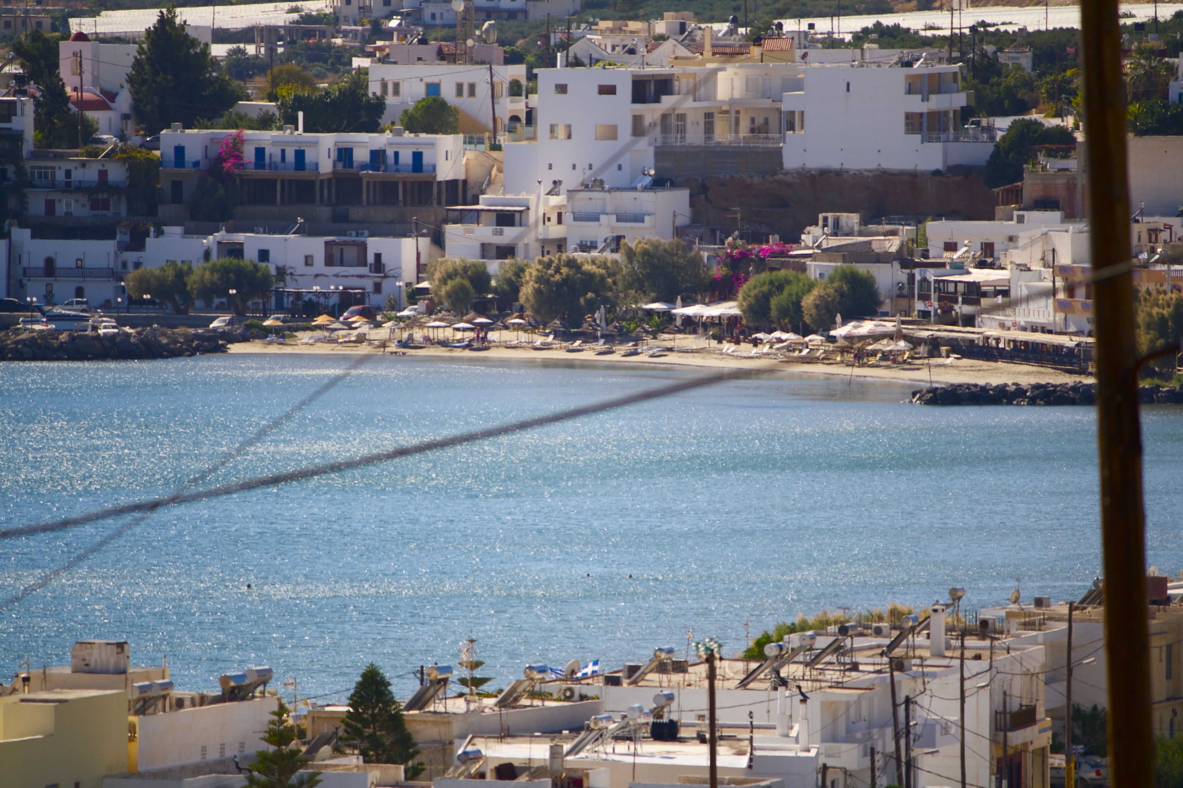 Un pueblo costero con edificios a lo largo del malecón, vista despejada del mar y un puente a lo lejos.