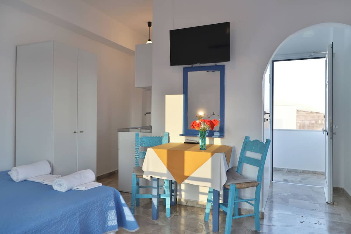 A hotel room with a bed, a table with a vase of flowers, a TV mounted on the wall, and a door leading to an outdoor balcony.