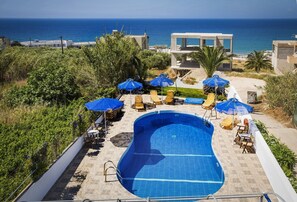 A swimming pool with lounge chairs and umbrellas, surrounded by greenery and overlooking the sea.