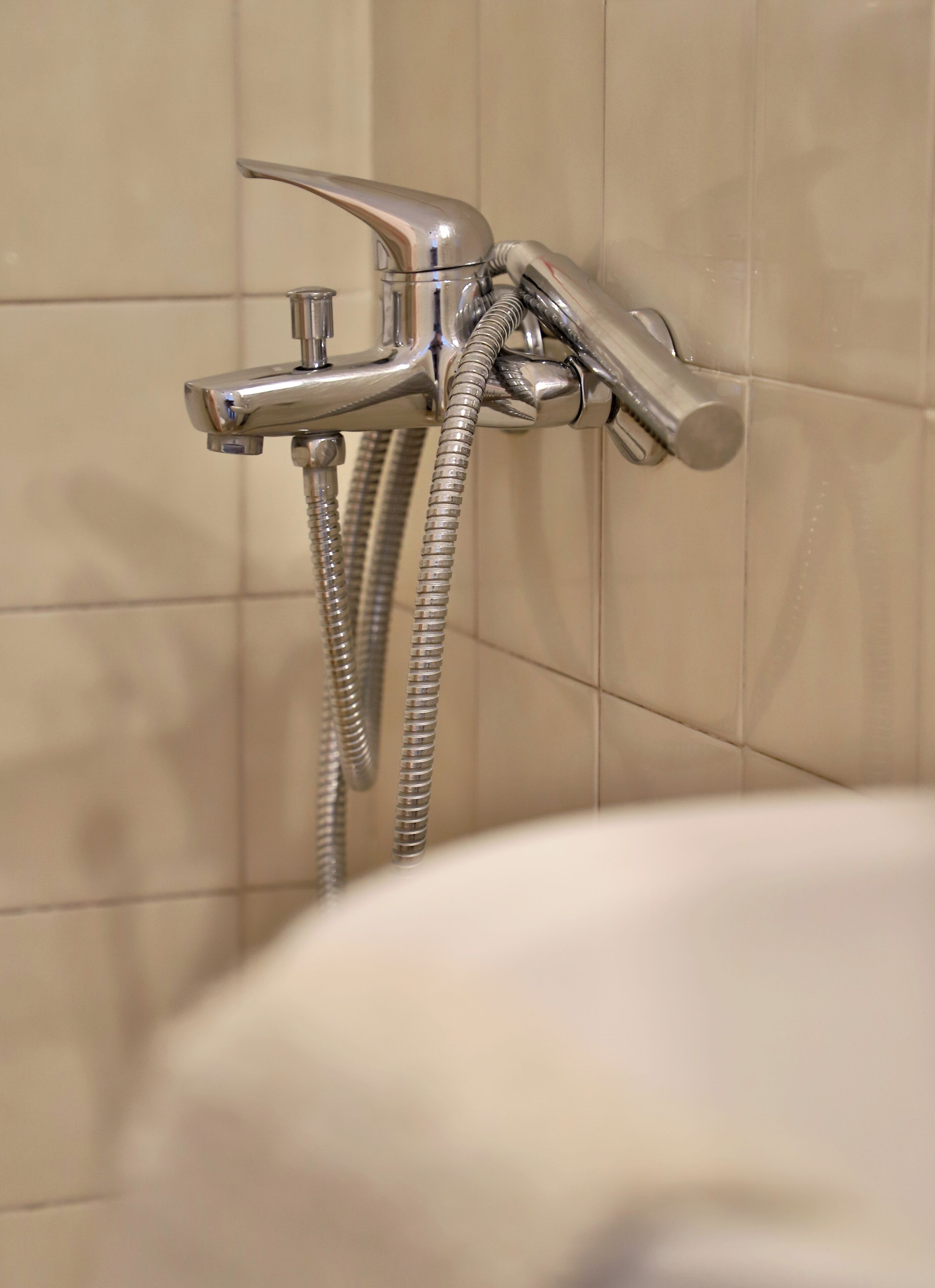 A bathroom with a wall-mounted shower faucet and hose.