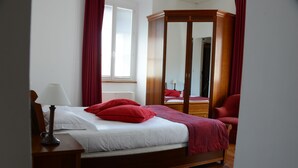 A bedroom with a wooden bed, red pillows, a wooden wardrobe, and a nightstand with a lamp.