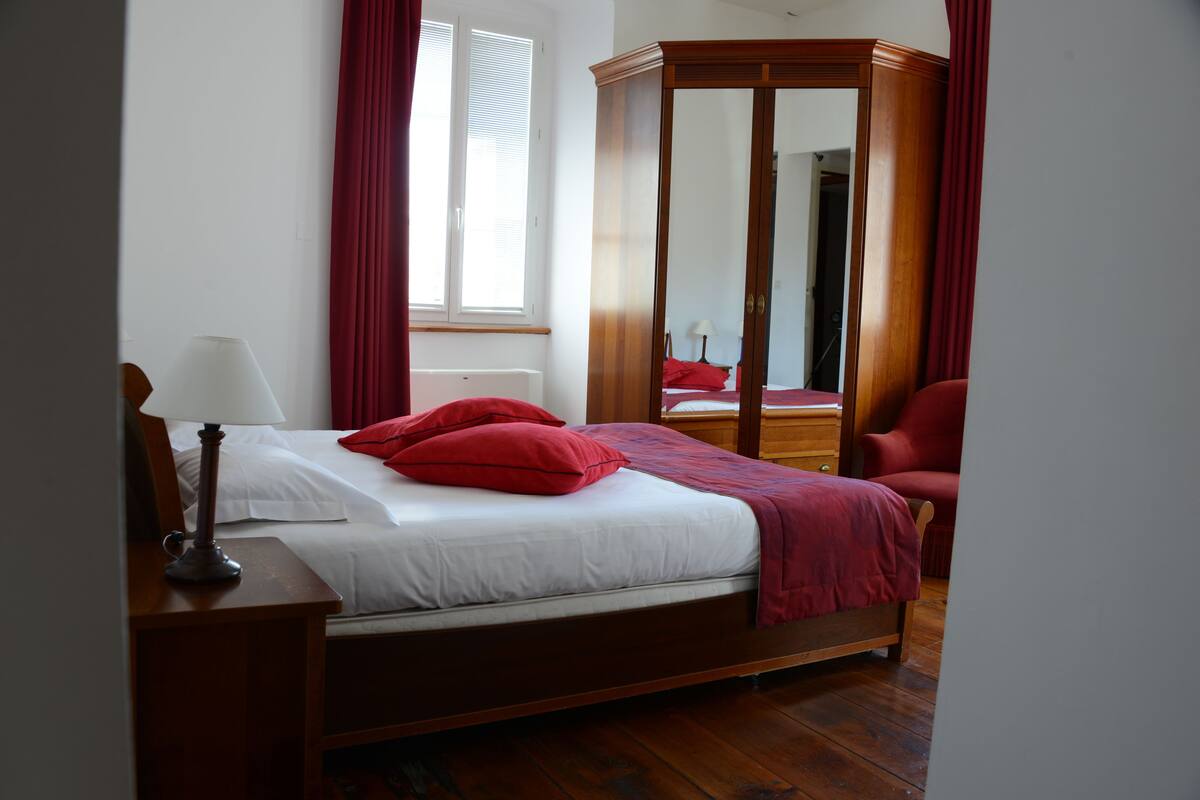 Een slaapkamer met een houten bed, rode kussens, een houten kledingkast en een nachtkastje met een lamp.