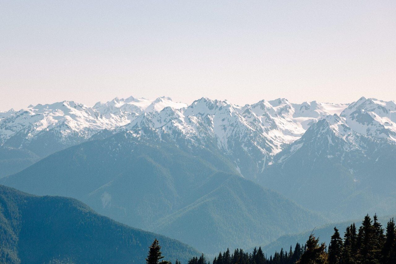 A mountain range with snow-capped peaks and dense forest at the base.