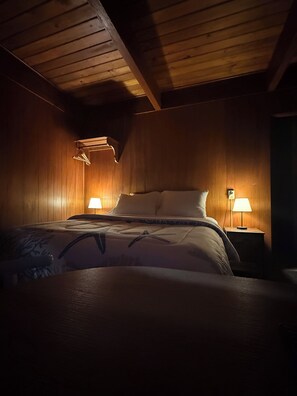Un dormitorio con paneles de madera, una cama, dos lámparas de noche y una lámpara colgante.