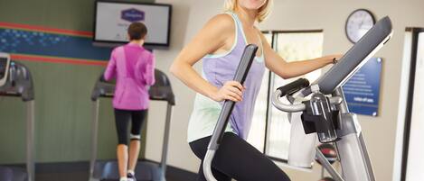 A gym with treadmills and a wall-mounted screen displaying a fitness program.