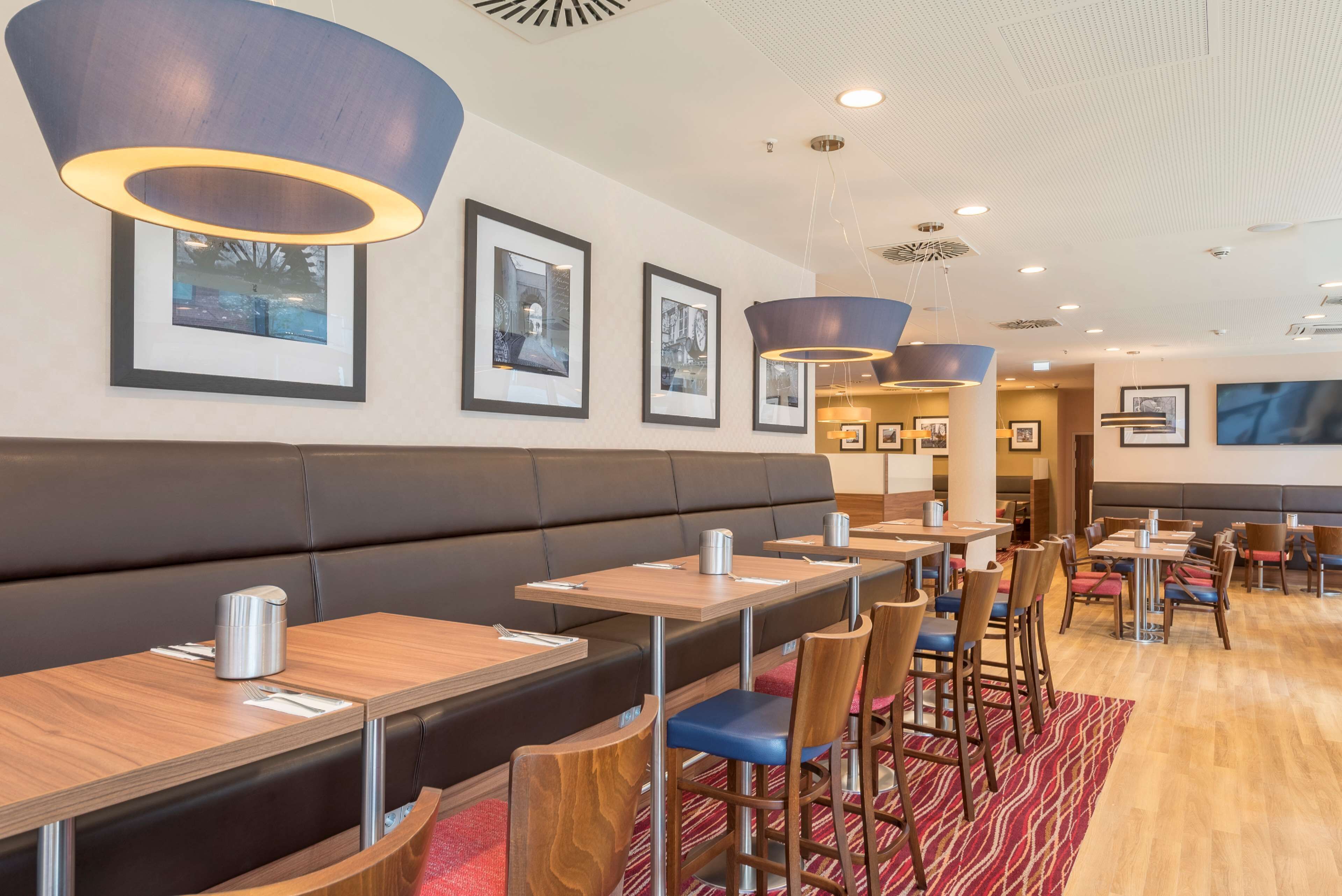 Ein Restaurant mit Sitzecken und Tischen, gerahmten Bildern an der Wand und modernen Leuchten.