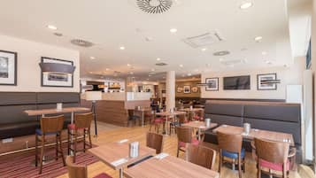 A modern restaurant with wooden tables and chairs, a central bar area, and framed pictures on the walls.
