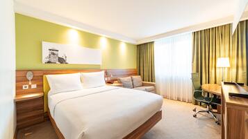 A hotel room with a large bed, a desk, a chair, a lamp, and a painting on the wall.