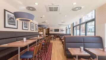 A modern restaurant with booths and tables, framed pictures on the walls, and large windows.