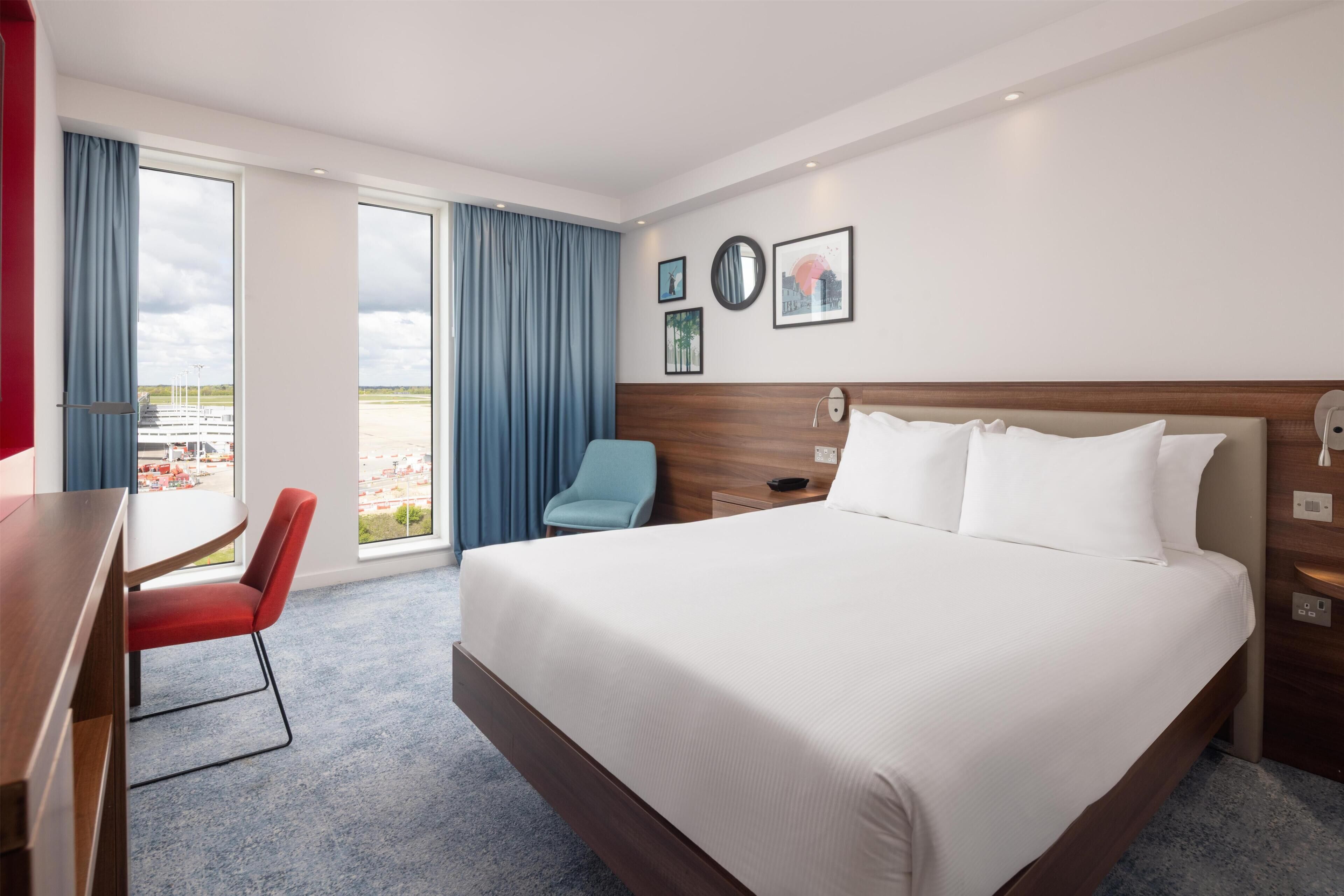 A hotel room with a large bed, a desk, a chair, and a view of the outside.