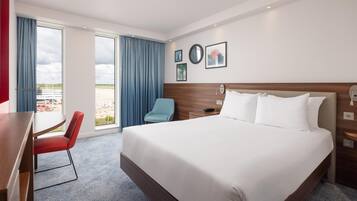 Habitación de hotel con una cama grande, un escritorio, una silla y vistas al exterior.